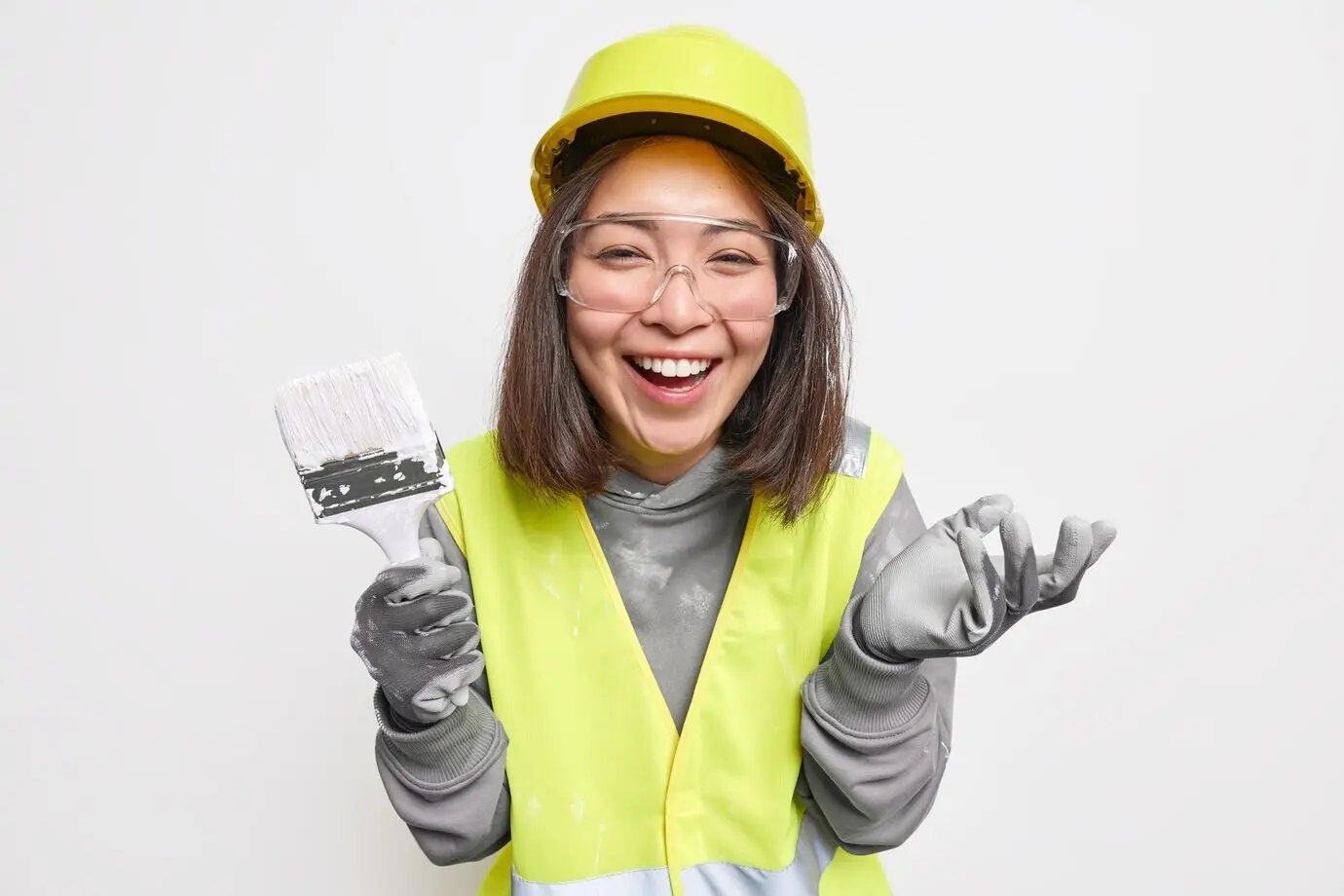 Eine Frau mit Schutzausrüstung und Uniform hält einen Pinsel, renoviert ein Haus und lächelt glücklich.